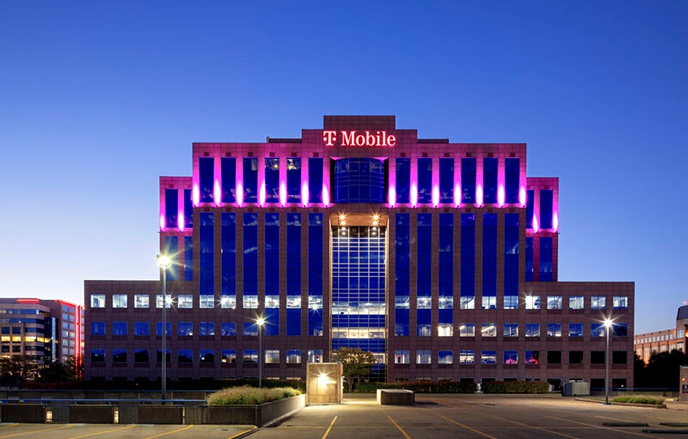 A modern office building lit in purple lights, featuring the T-Mobile logo prominently at the top center.